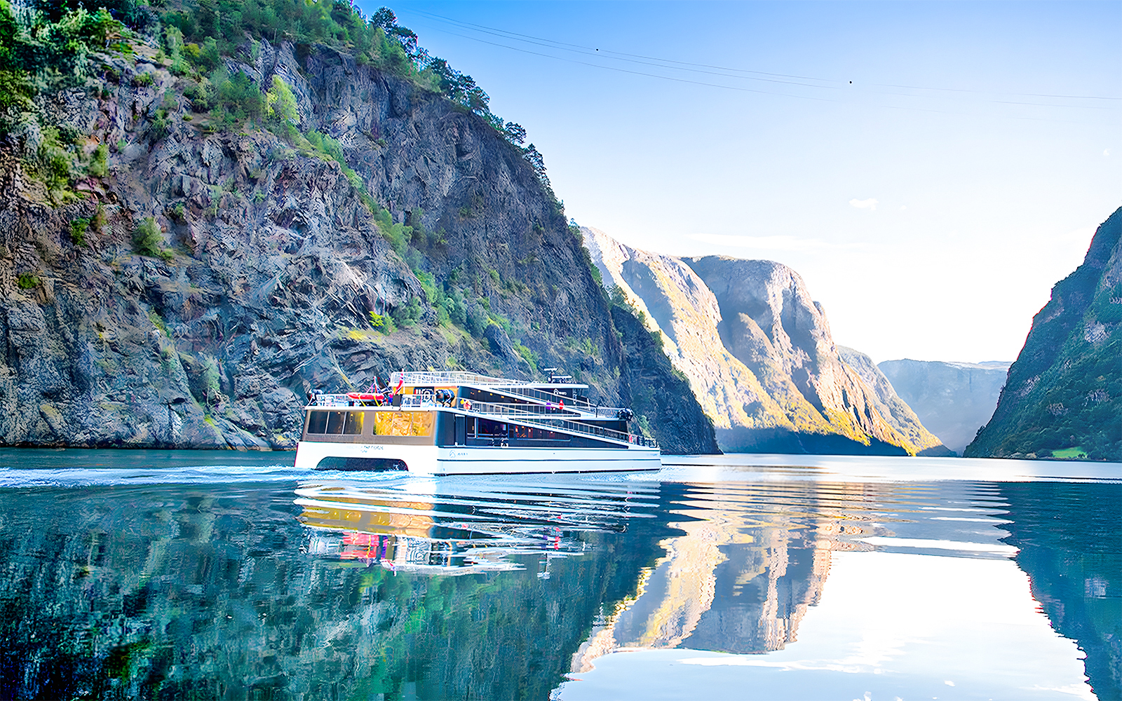 Cruise ship on Nærøyfjord surrounded by steep cliffs and calm water.