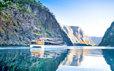 Cruise ship on Nærøyfjord surrounded by steep cliffs and calm water.