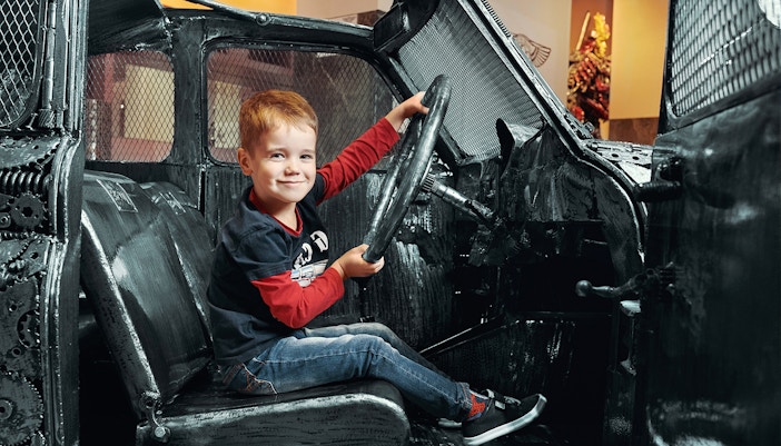 Child sitting in a steel car sculpture at the Gallery of Steel Figures, Prague.