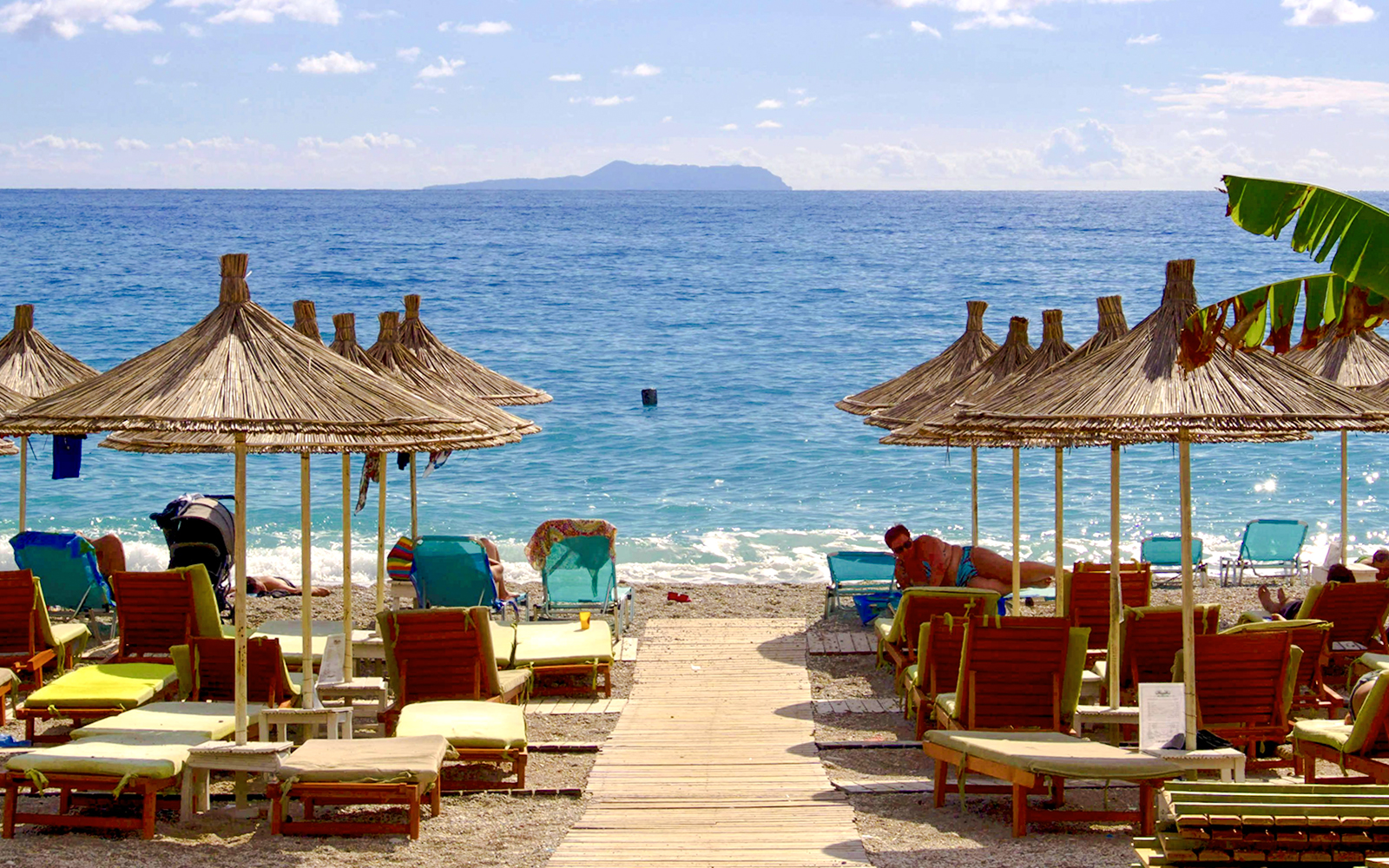 Sun loungers and straw umbrellas on Dhërmi beach, Albania, with clear blue sea.