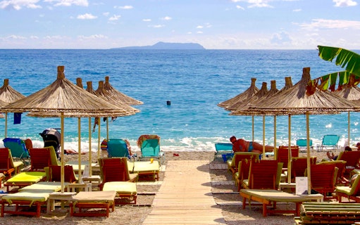 Sun loungers and straw umbrellas on Dhërmi beach, Albania, with clear blue sea.