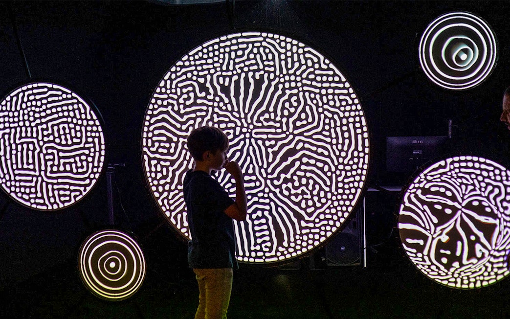 Child observing illuminated circular patterns at Lumia Gallery light art exhibition.