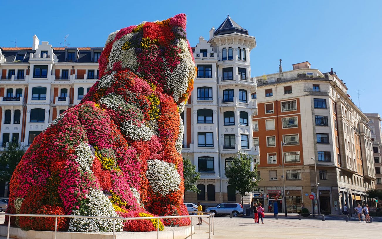 Floral sculpture of a dog at Guggenheim Museum Bilbao, with surrounding architecture.