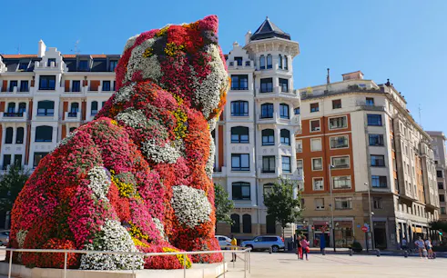 Floral sculpture of a dog at Guggenheim Museum Bilbao, with surrounding architecture.