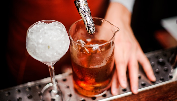 Cocktail with ice and spooky finger stirrer on bar counter.
