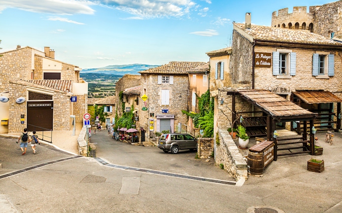 Charming village street in Sault, France, with stone buildings and distant mountain views.