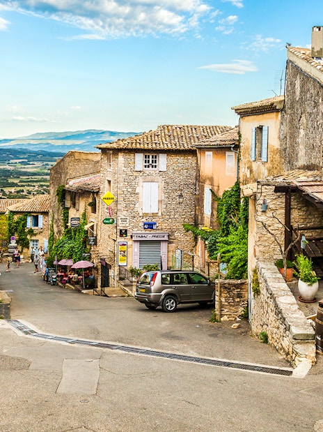 Charming village street in Sault, France, with stone buildings and distant mountain views.