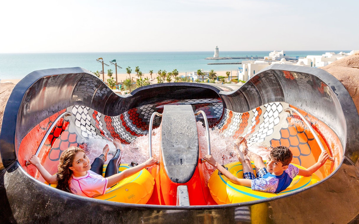 Riders on King Cobra water slide in Doha with ocean view in background.