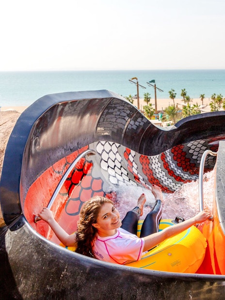 Riders on King Cobra water slide in Doha with ocean view in background.