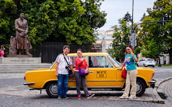 Tourists posing with a yellow Fiat 125p near the Józef Piłsudski statue in Warsaw.