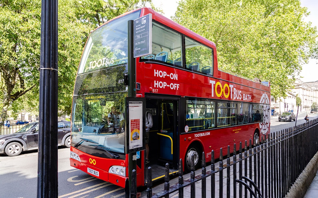 Red Toot Bus for hop-on hop-off tour in Bath, parked on a tree-lined street.