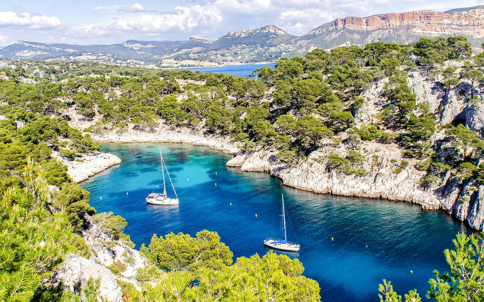 Sailboats in a turquoise inlet surrounded by cliffs and trees at Calanques National Park, Marseille.