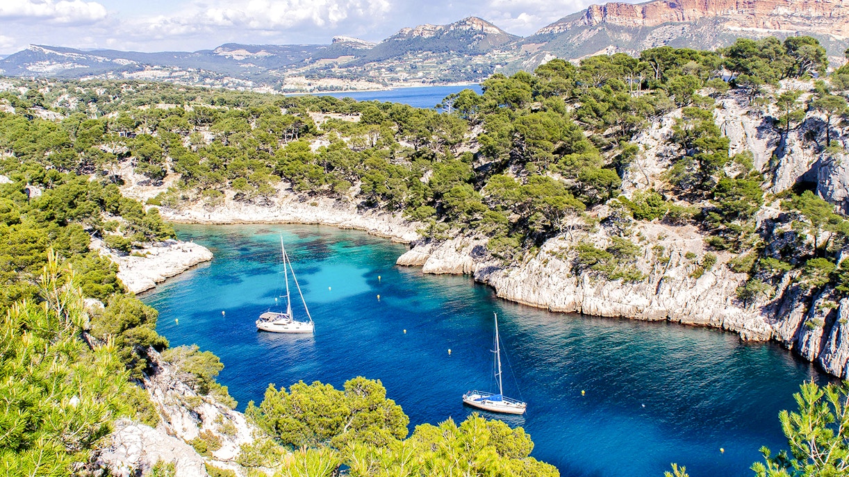 Sailboats in a turquoise inlet surrounded by cliffs and trees at Calanques National Park, Marseille.