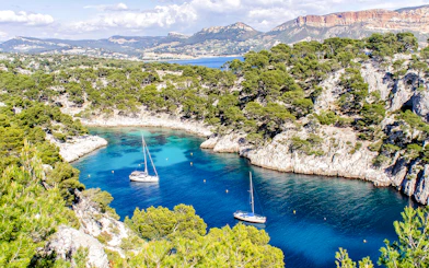 Sailboats in a turquoise inlet surrounded by cliffs and trees at Calanques National Park, Marseille.