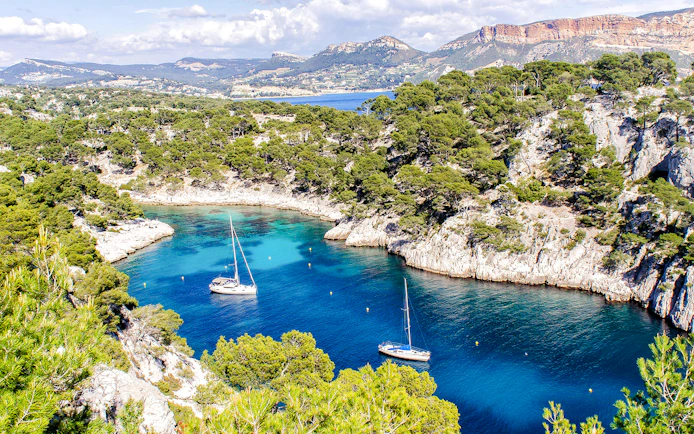 Sailboats in a turquoise inlet surrounded by cliffs and trees at Calanques National Park, Marseille.