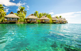 Overwater bungalows with thatched roofs in Bimini, Bahamas, surrounded by clear blue water.