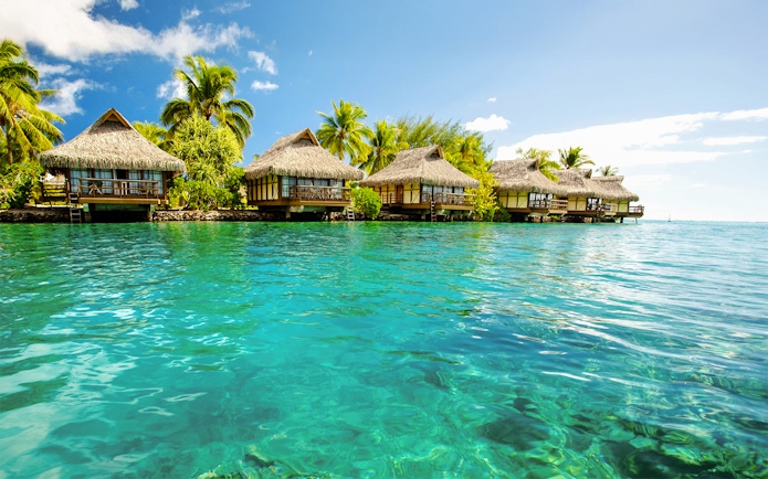 Overwater bungalows with thatched roofs in Bimini, Bahamas, surrounded by clear blue water.