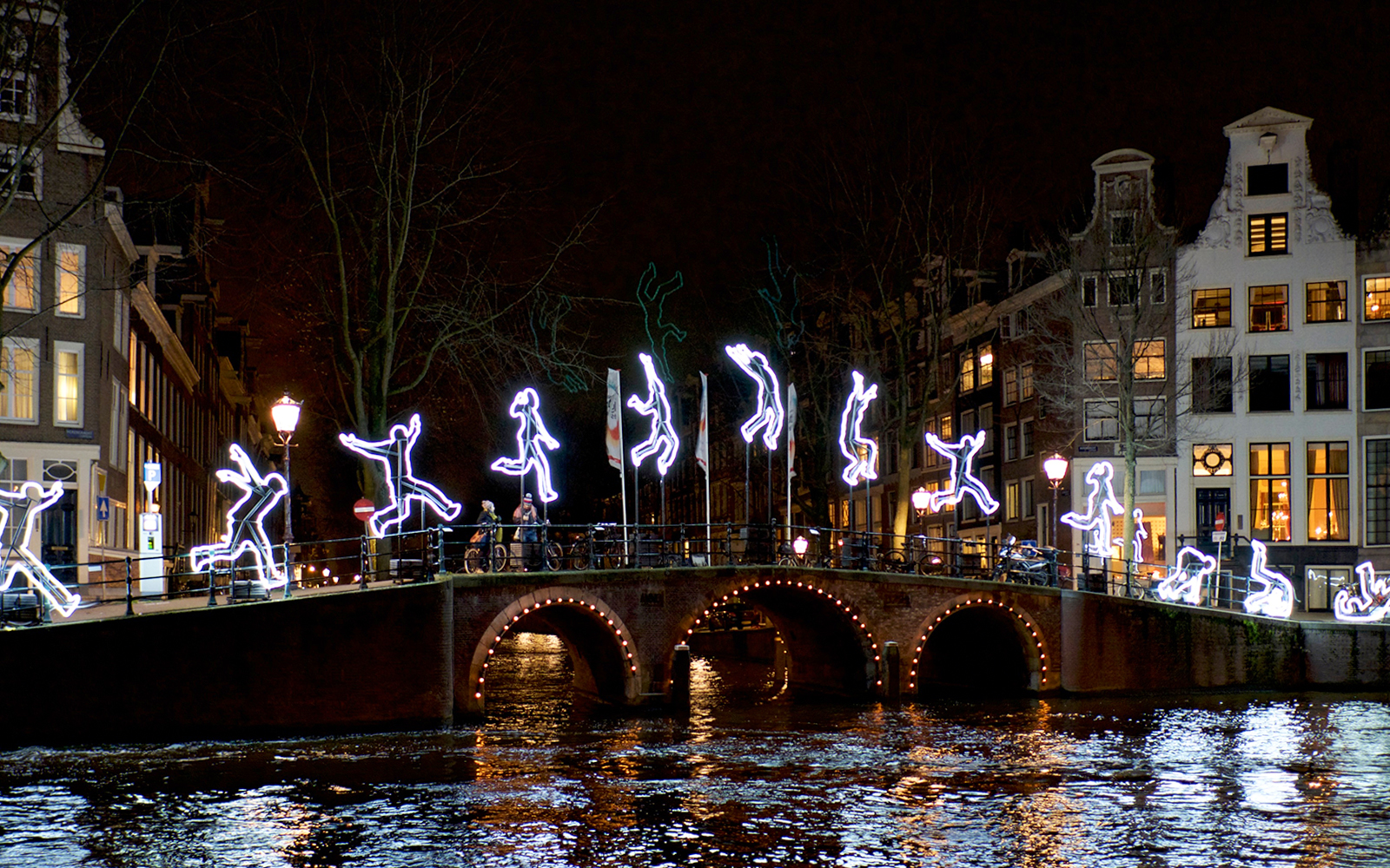 Amsterdam canal bridge with illuminated figures during Light Festival cruise.