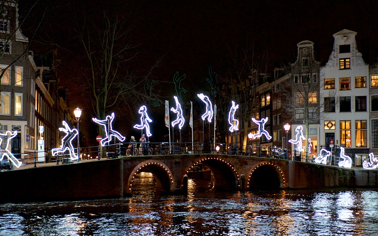 Amsterdam canal bridge with illuminated figures during Light Festival cruise.