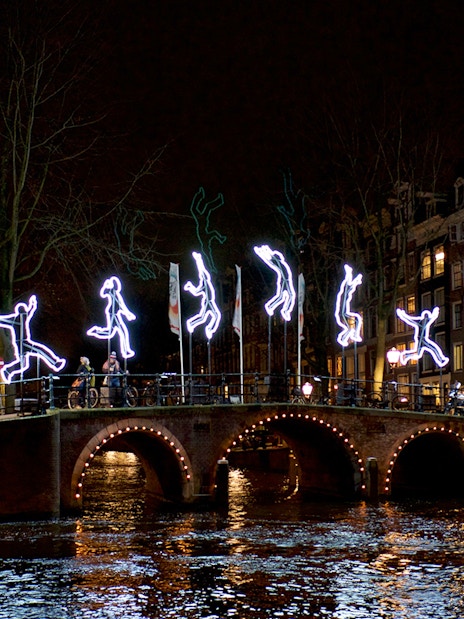 Amsterdam canal bridge with illuminated figures during Light Festival cruise.