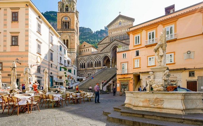 Amalfi Cathedral and fountain in Cathedral Square, Italy, with outdoor café seating.