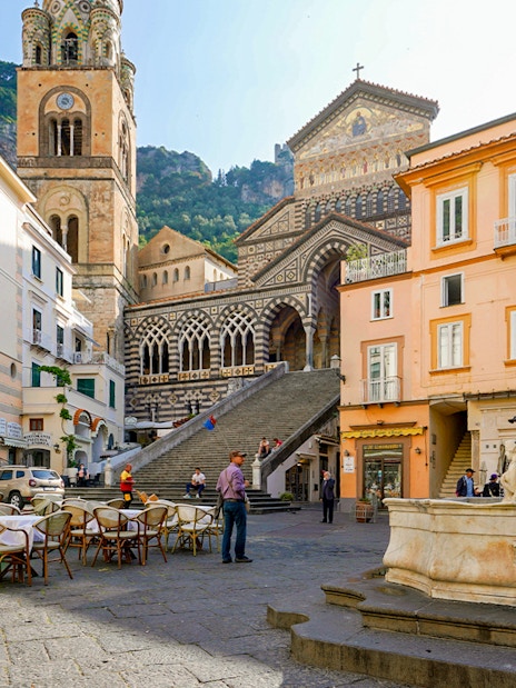 Amalfi Cathedral and fountain in Cathedral Square, Italy, with outdoor café seating.