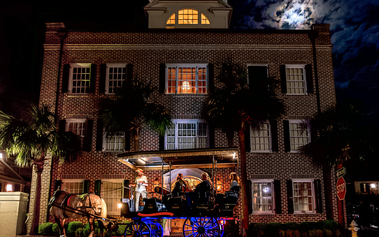 Charleston horse-drawn carriage tour passing historic brick building at night.