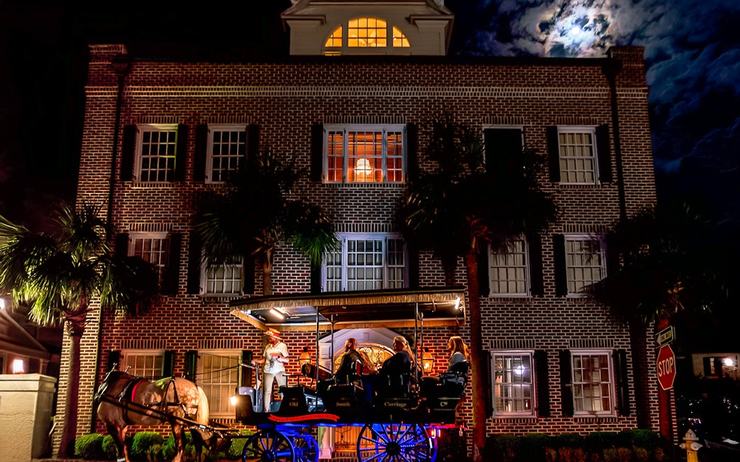 Charleston horse-drawn carriage tour passing historic brick building at night.
