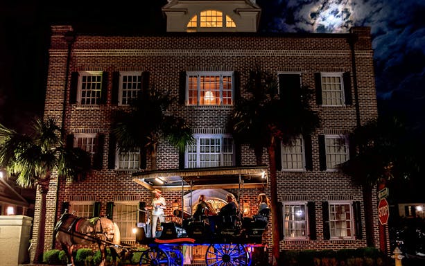 Charleston horse-drawn carriage tour passing historic brick building at night.