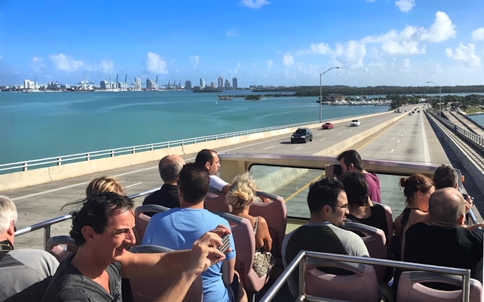 Open-top bus tour crossing a bridge with Miami skyline in the background.