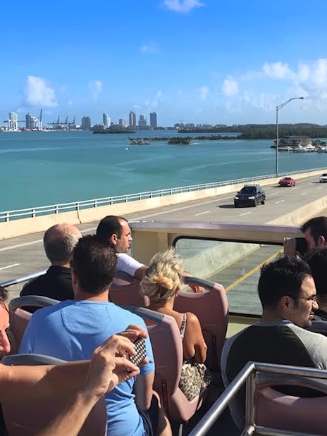 Open-top bus tour crossing a bridge with Miami skyline in the background.