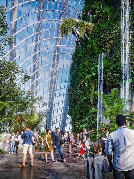 Visitors at Brach Falls in a lush indoor garden with dinosaur sculptures and waterfalls.