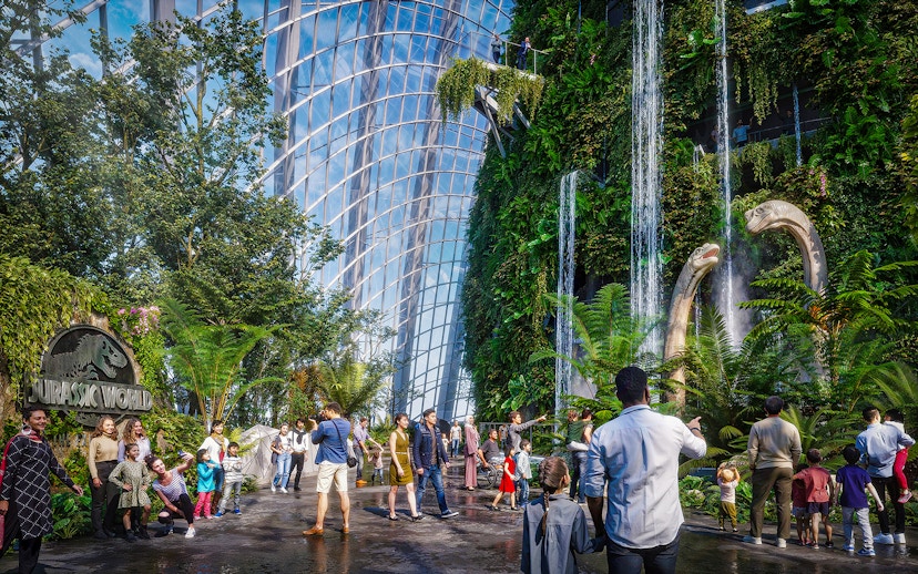 Visitors at Brach Falls in a lush indoor garden with dinosaur sculptures and waterfalls.