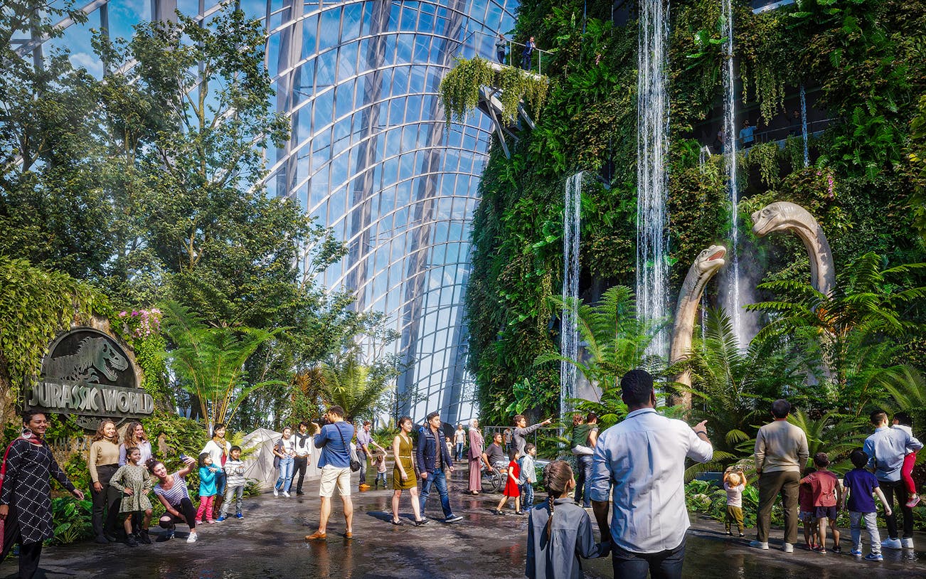 Visitors at Brach Falls in a lush indoor garden with dinosaur sculptures and waterfalls.