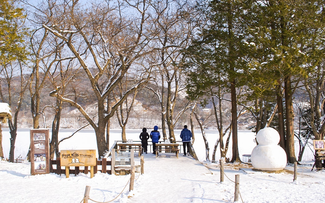 People walking on snowy path with snowman on Nami Island, South Korea.