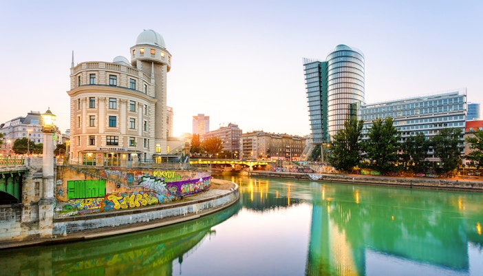 The image shows the Urania building in Vienna, Austria, reflected in the Donaukanal Danube Canal