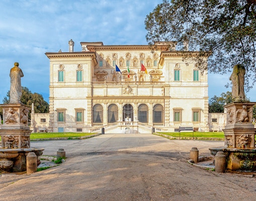 Villa Borghese facade with statues and trees during sunset in Rome, Italy.