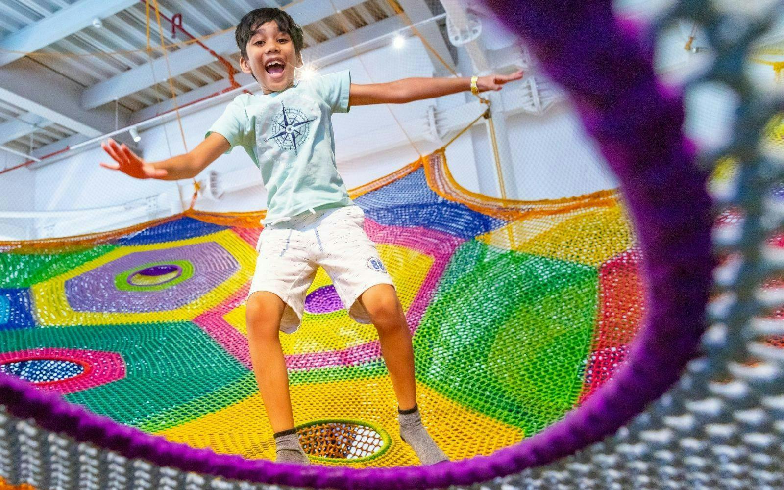 Child jumping on colorful net at OliOli Children's Museum.