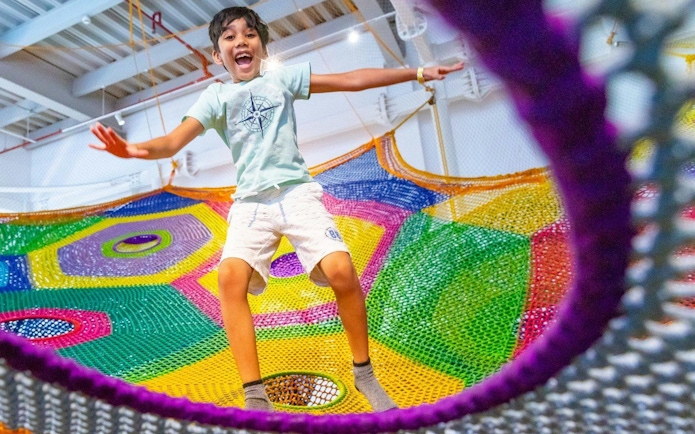Child jumping on colorful net at OliOli Children's Museum.