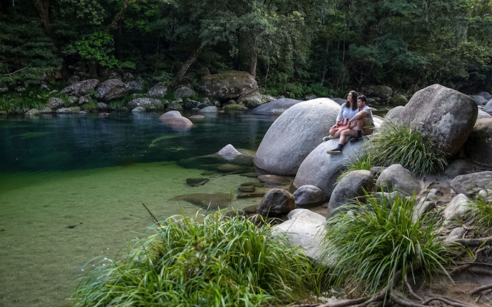 Couple sitting on rocks by a clear river in Daintree Rainforest, Australia.