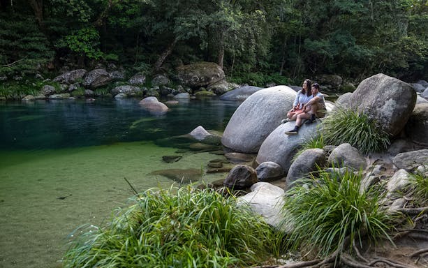 Couple sitting on rocks by a clear river in Daintree Rainforest, Australia.