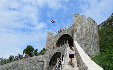 Woman climbing the Walls of Ston in Ston, Croatia, with people on the battlements.