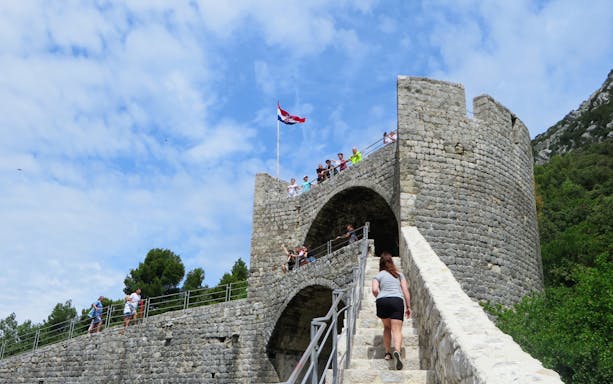 Woman climbing the Walls of Ston in Ston, Croatia, with people on the battlements.