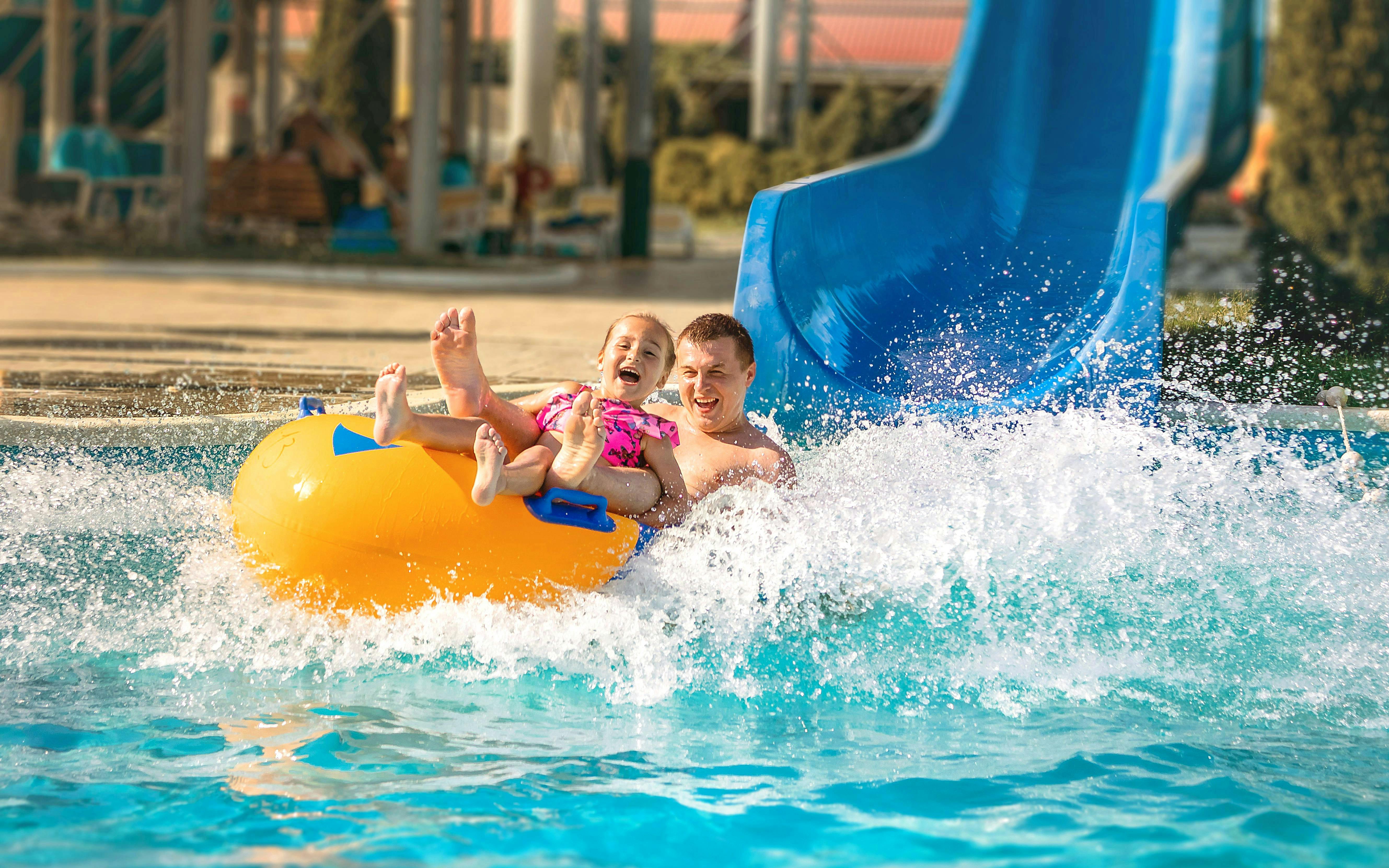 Father and child on a yellow raft sliding down a blue water slide at Agadir Aqua Park.