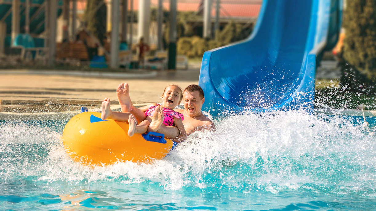 Father and child on a yellow raft sliding down a blue water slide at Agadir Aqua Park.