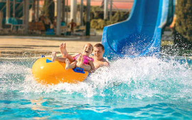 Father and child on a yellow raft sliding down a blue water slide at Agadir Aqua Park.