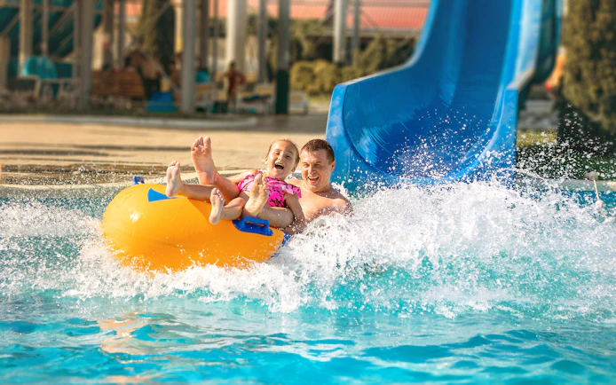 Father and child on a yellow raft sliding down a blue water slide at Agadir Aqua Park.