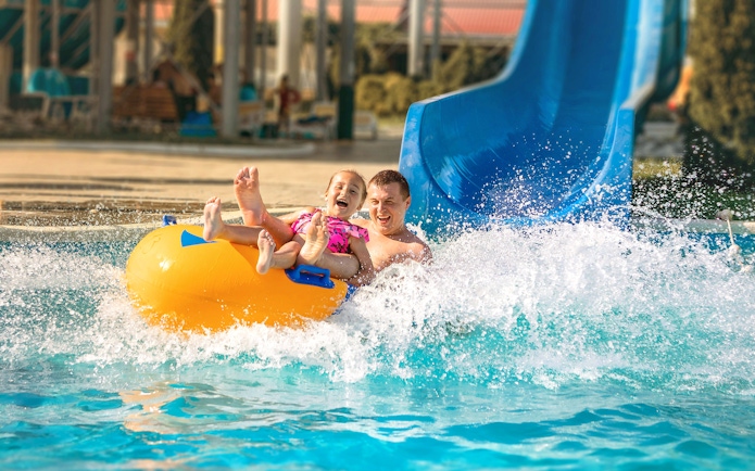 Father and child on a yellow raft sliding down a blue water slide at Agadir Aqua Park.