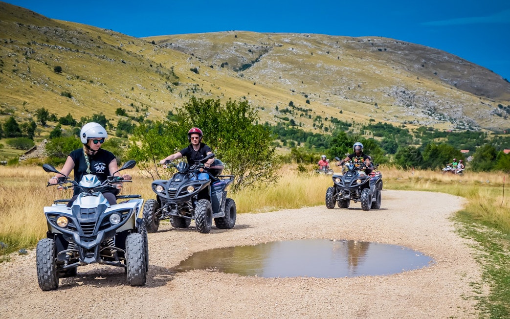 ATV riders on a dirt path in Cappadocia with scenic hills in the background.