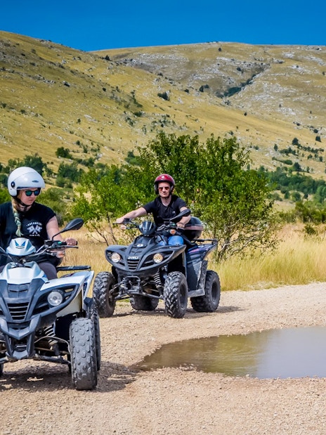 ATV riders on a dirt path in Cappadocia with scenic hills in the background.